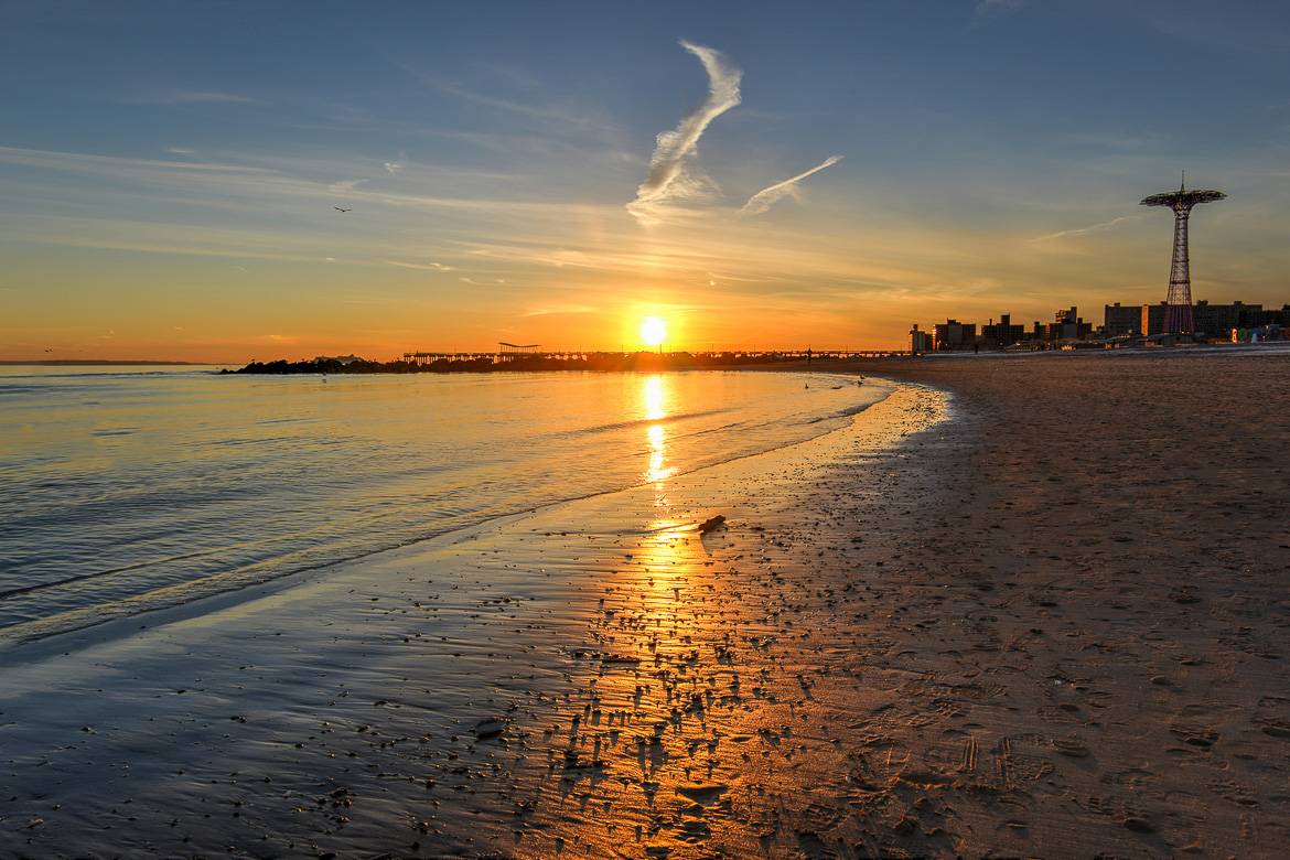 A sunset over Coney Island, with the classic rides of Luna Park on the right.