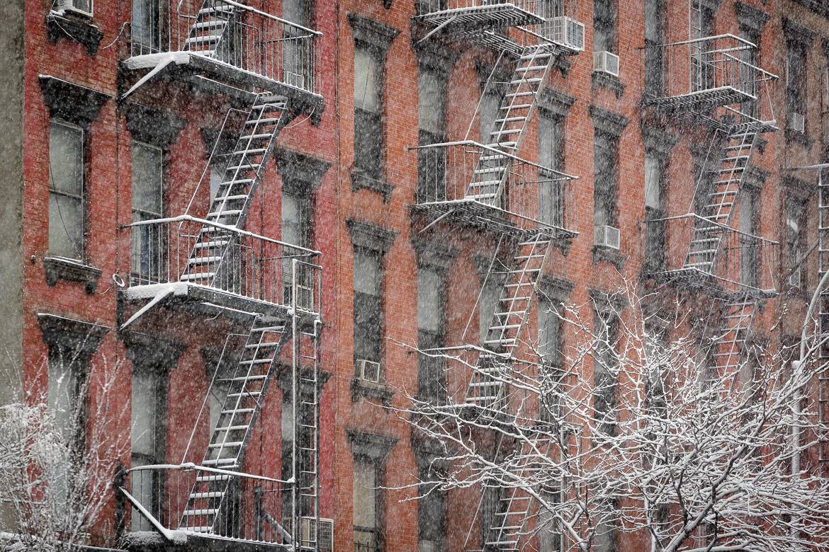Image of a row of low-rise buildings in New York with fire escapes covered in snow