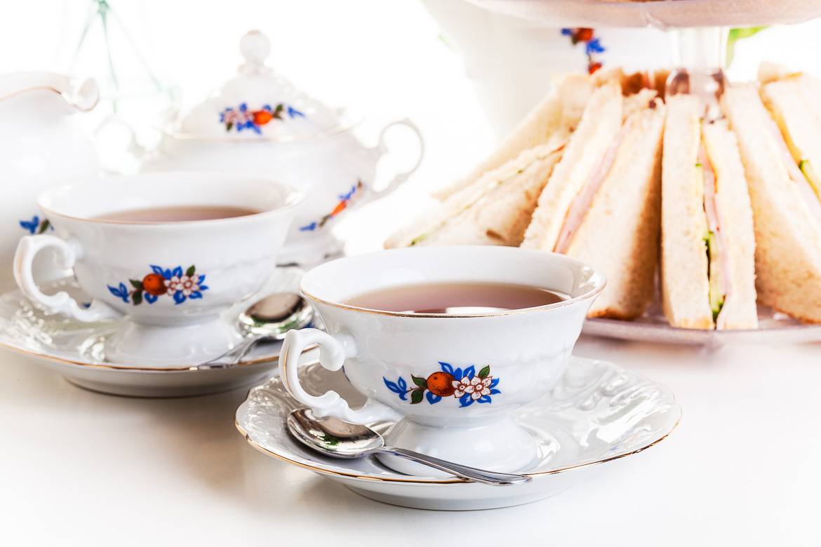 Image of two white teacups and a plate of finger sandwiches