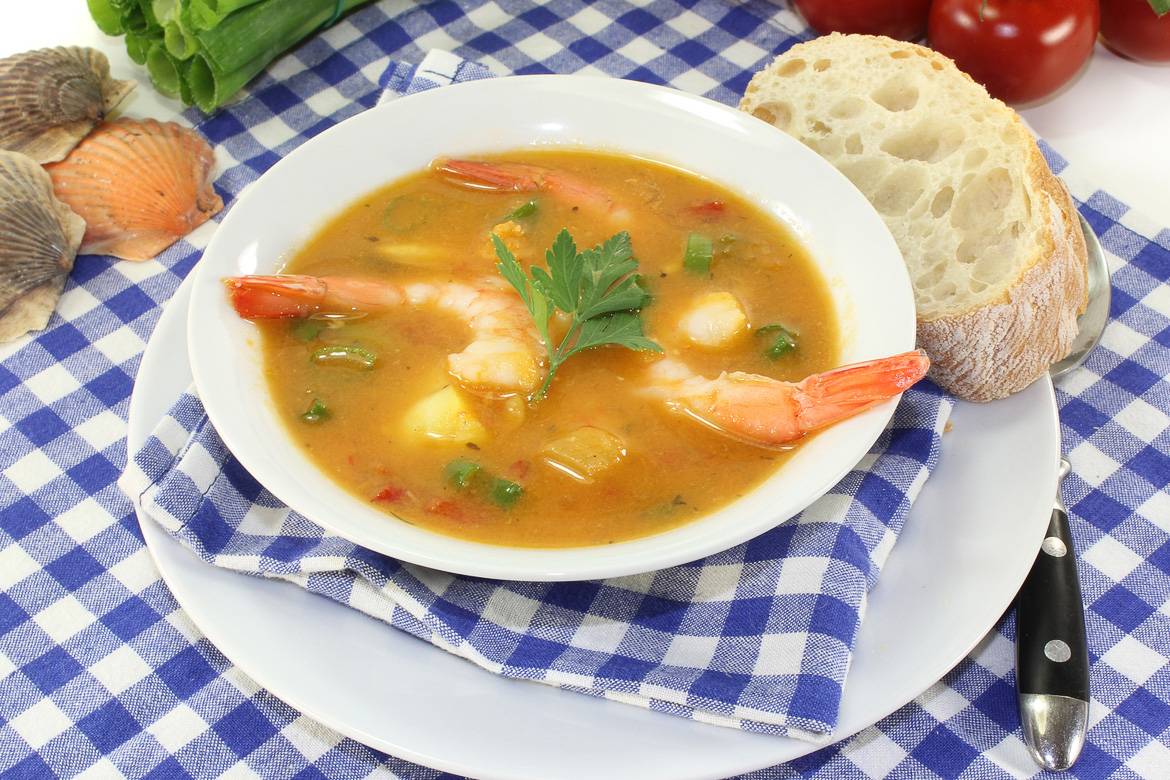 Image of a bowl of bouillabaisse and a slice of bread on a blue and white checked tablecloth