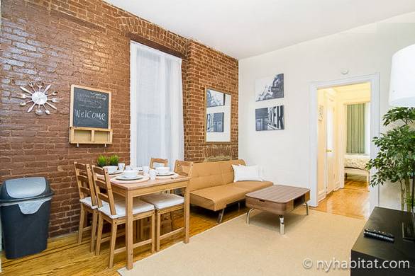 Image of living room with exposed brick, furnished with a futon and dining table in NY-16309