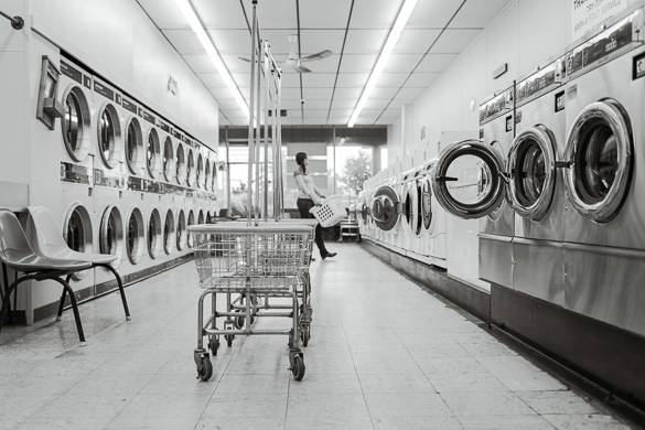 Image of person standing in laundromat with rows of washers, dryers and laundry carts