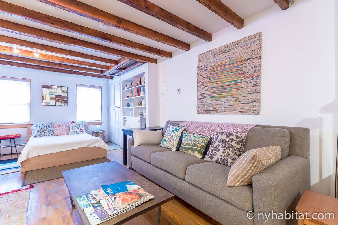 Image of living area of NY-10856 studio rental with bed, sofa, and artwork.