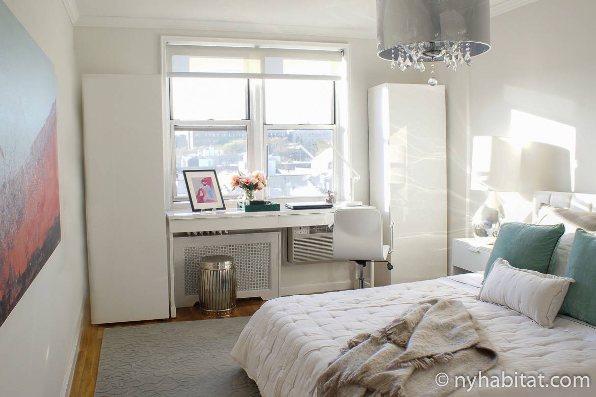 Image of bedroom in NY-17527 with queen-sized bed, desk, chandelier and window.