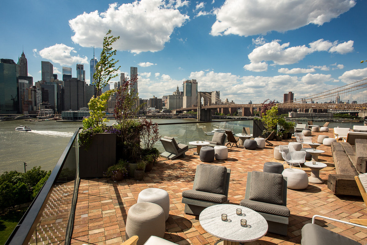 Image of the 1 Hotel Brooklyn Bridge rooftop bar with views of the East River and Manhattan skyline.