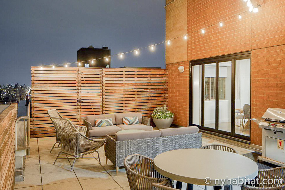 Image of rooftop lounge with patio furniture and string lights at furnished apartment NY-17339
