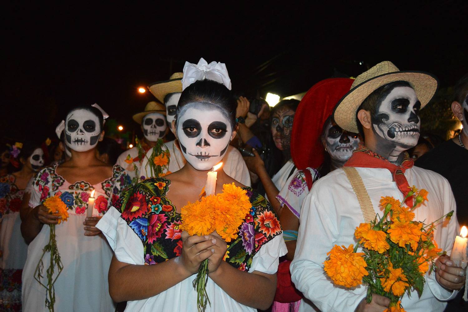 Image of people with skeleton face paint carrying candles for Día de los muertos.