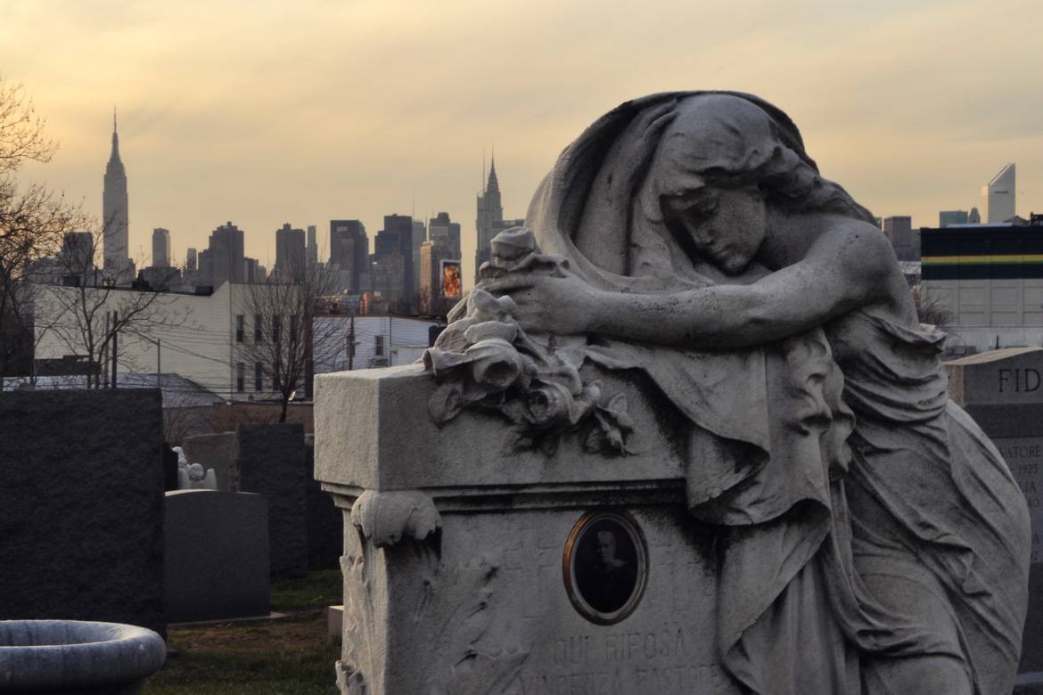 Image of grave with statue in Cavalry Cemetery in Queens, New York at sunset.