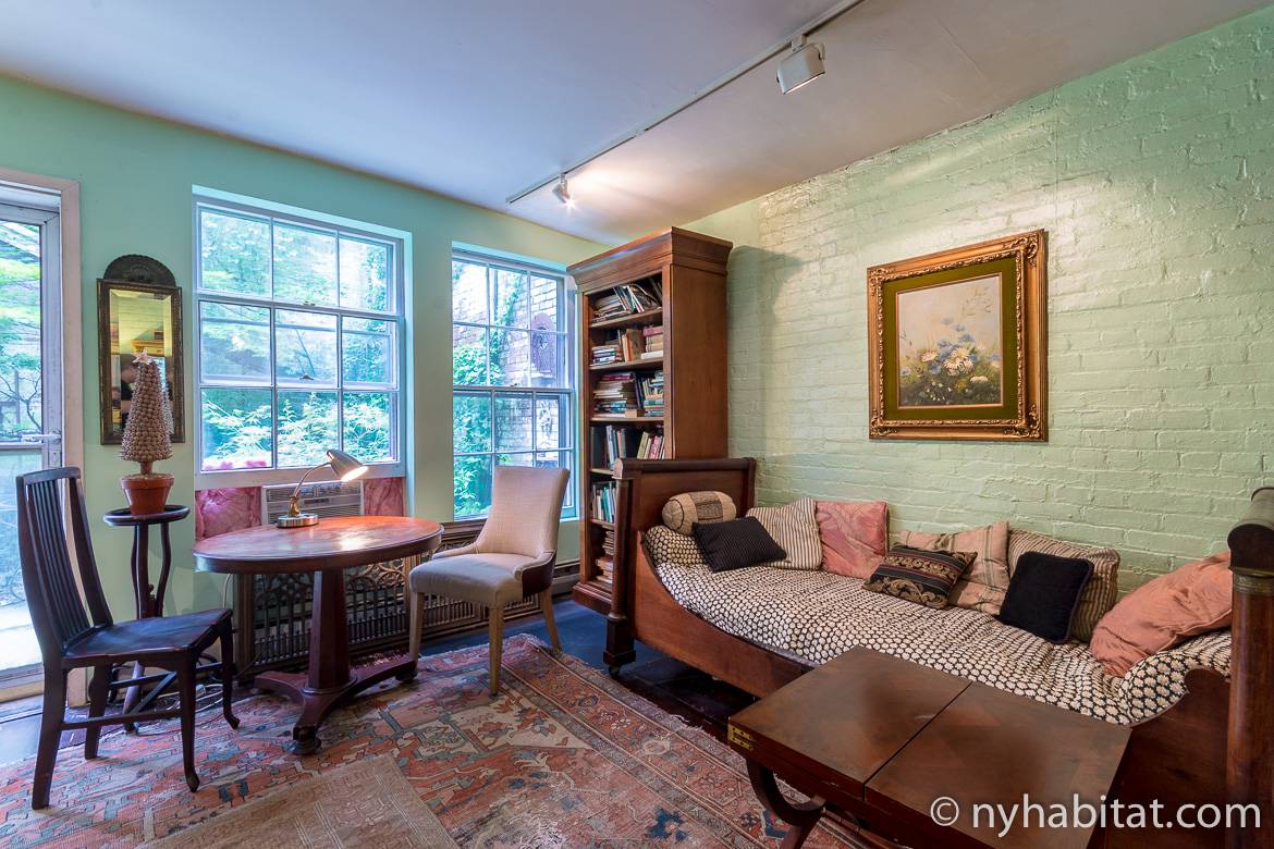 Image of living area of NY-15343 in Chelsea with antique sofa, table and chairs and wooden bookshelf.