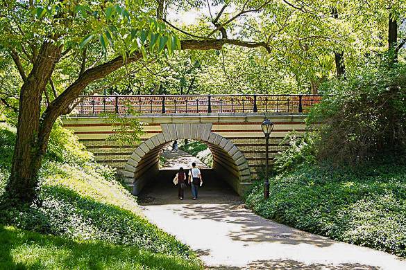 Image of a couple walking through one of Central Park’s many arches in the summertime