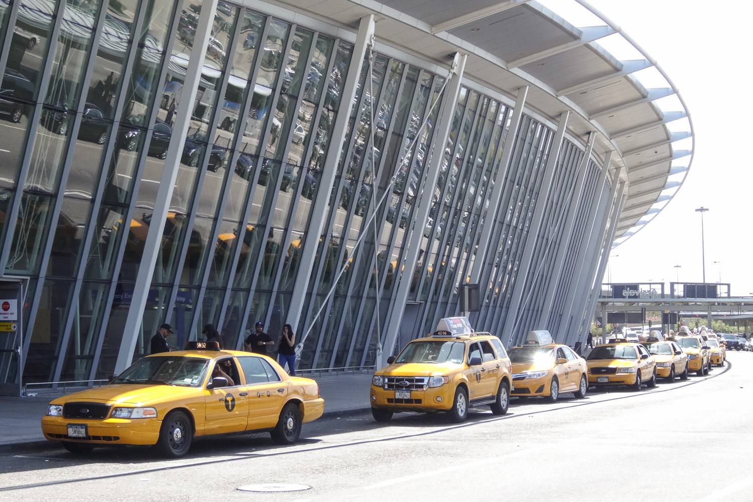 Image of NYC yellow taxis waiting to pick up riders at the curb of JFK airport.