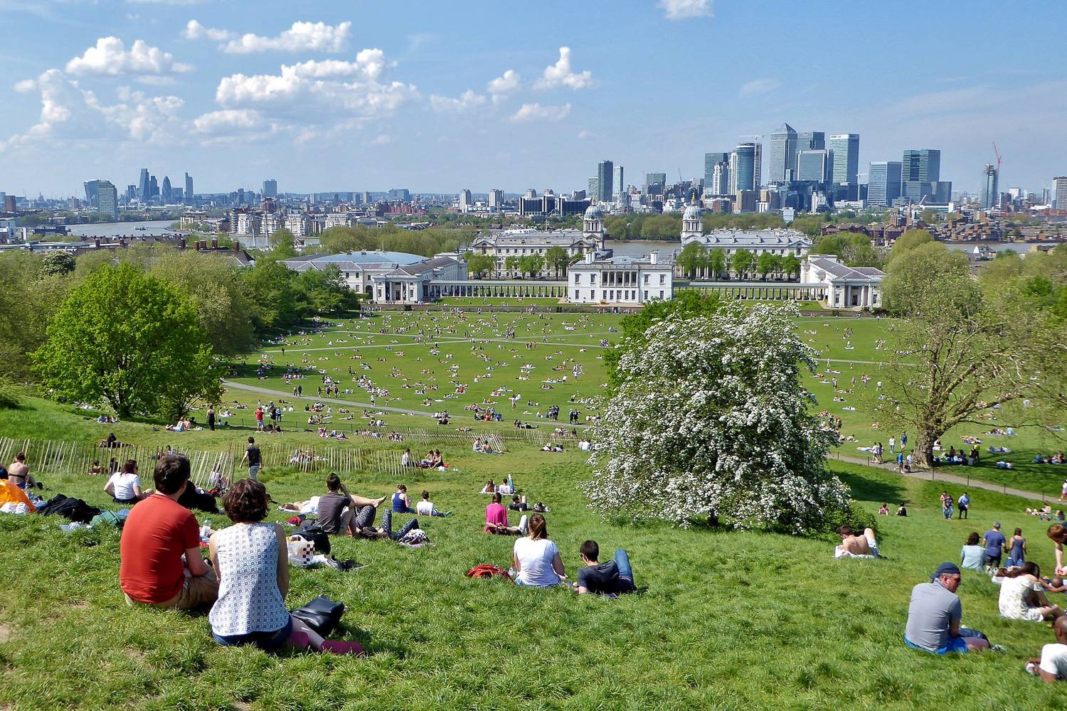 Image of people sitting on the hill in Greenwich Park facing London’s skyline on a sunny spring day.