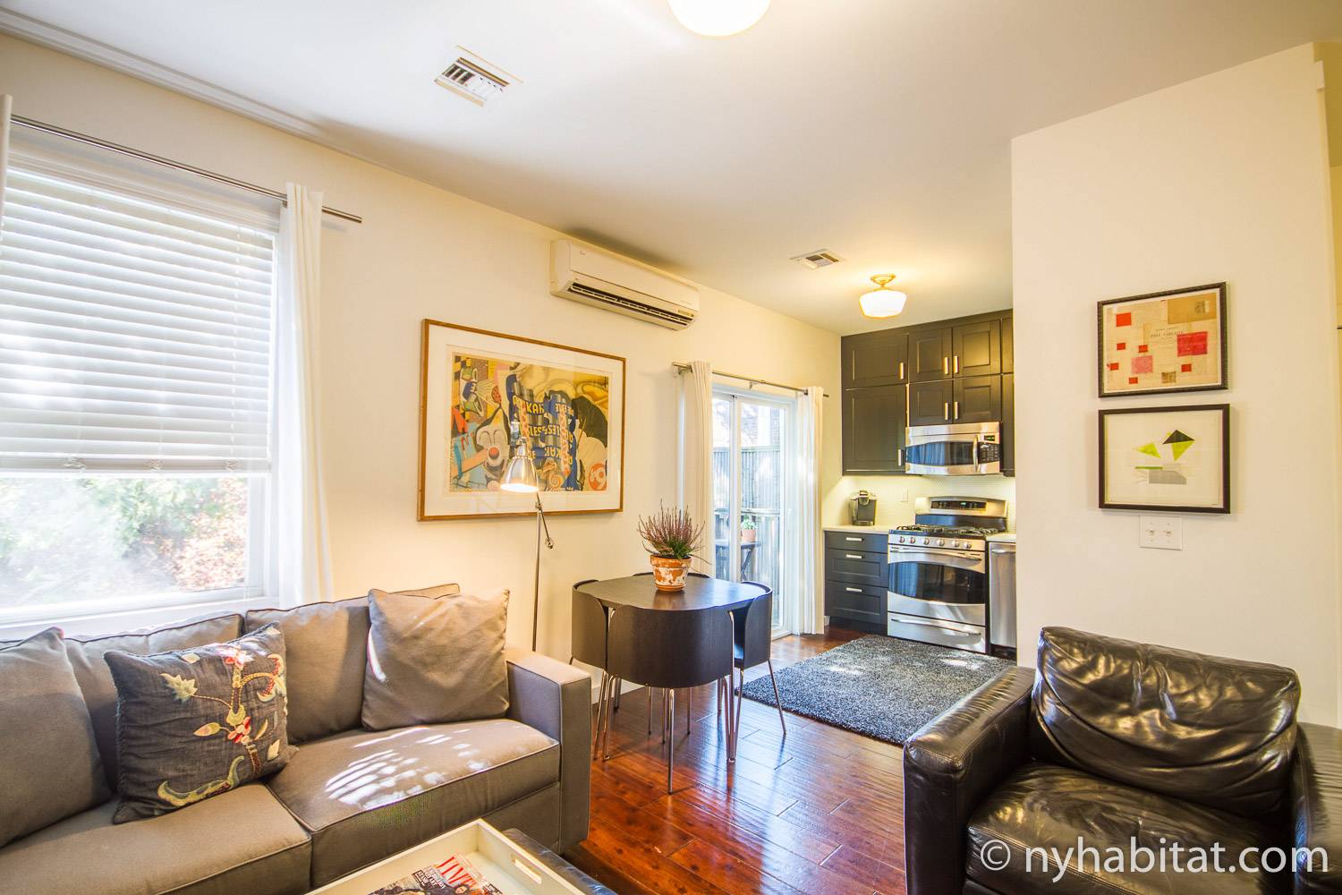 Image of living and kitchen area in NY-15411 with leather chair, sofa, small dining table, and stove.