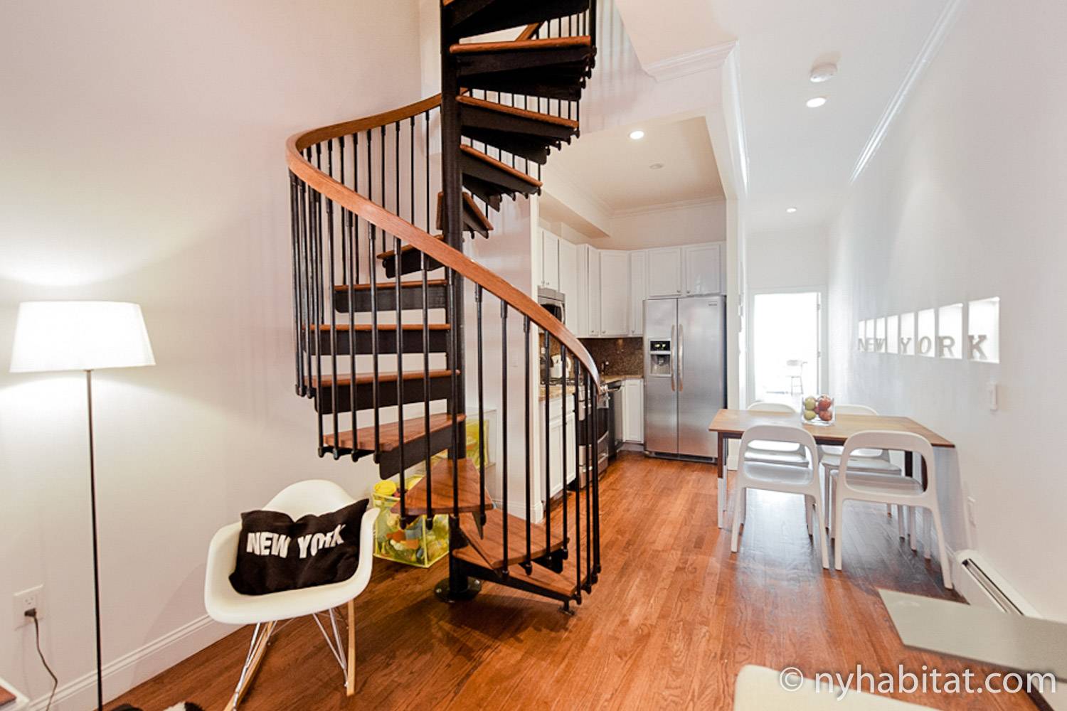 Image of living and kitchen area in NY-15593 with spiral staircase, dining table and chairs, and refrigerator.