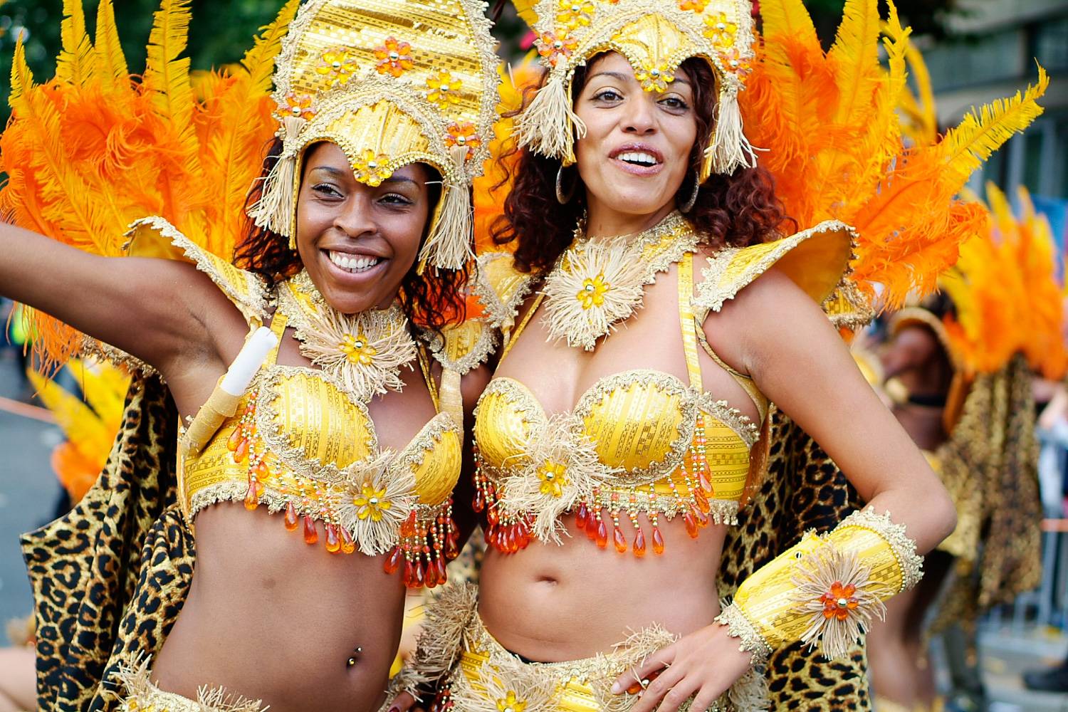 Image of two women in elaborate yellow costumes dancing in the Notting Hill Carnival.