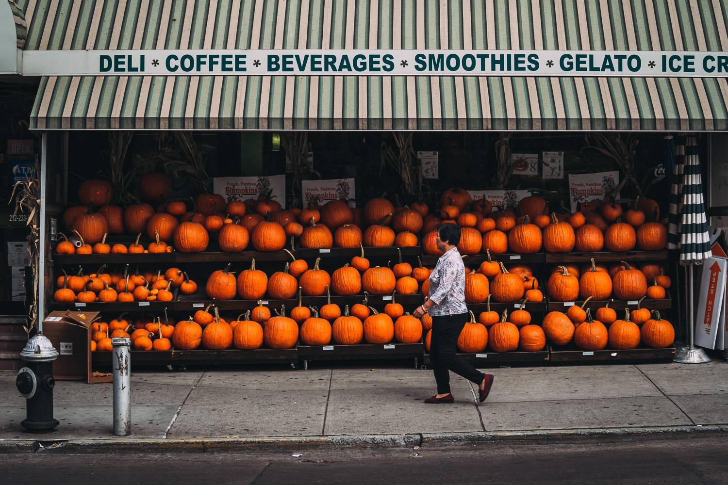 Image of a woman walking by a deli in Chinatown selling pumpkins.