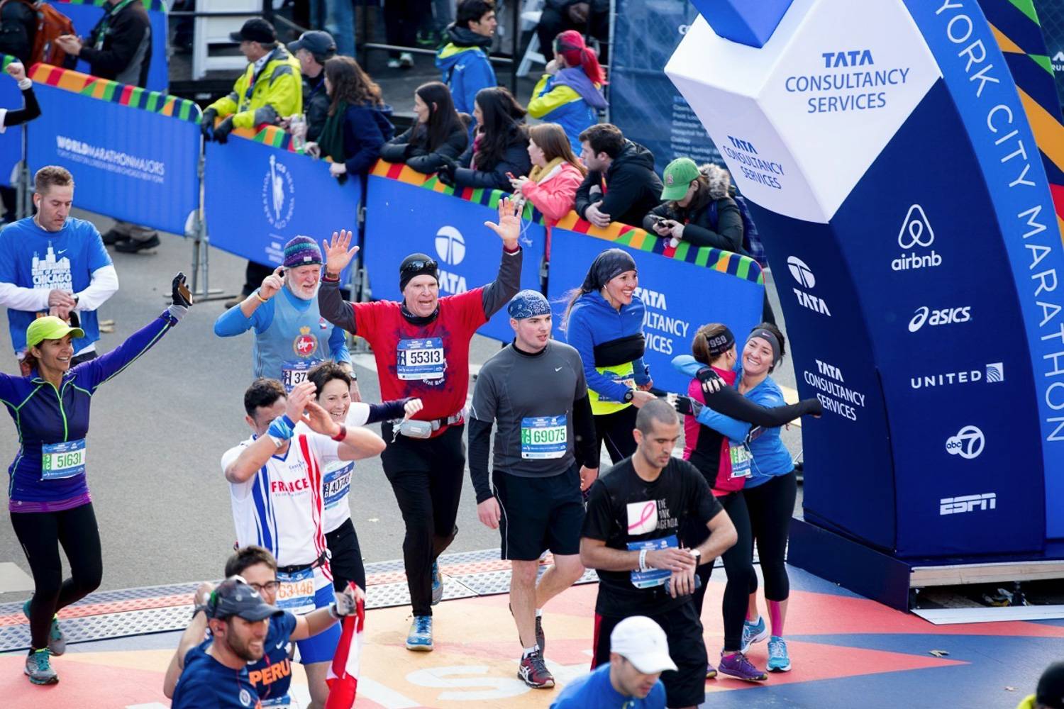 Image of runners cheering and hugging each other as they race past the finish line in the New York City Marathon.