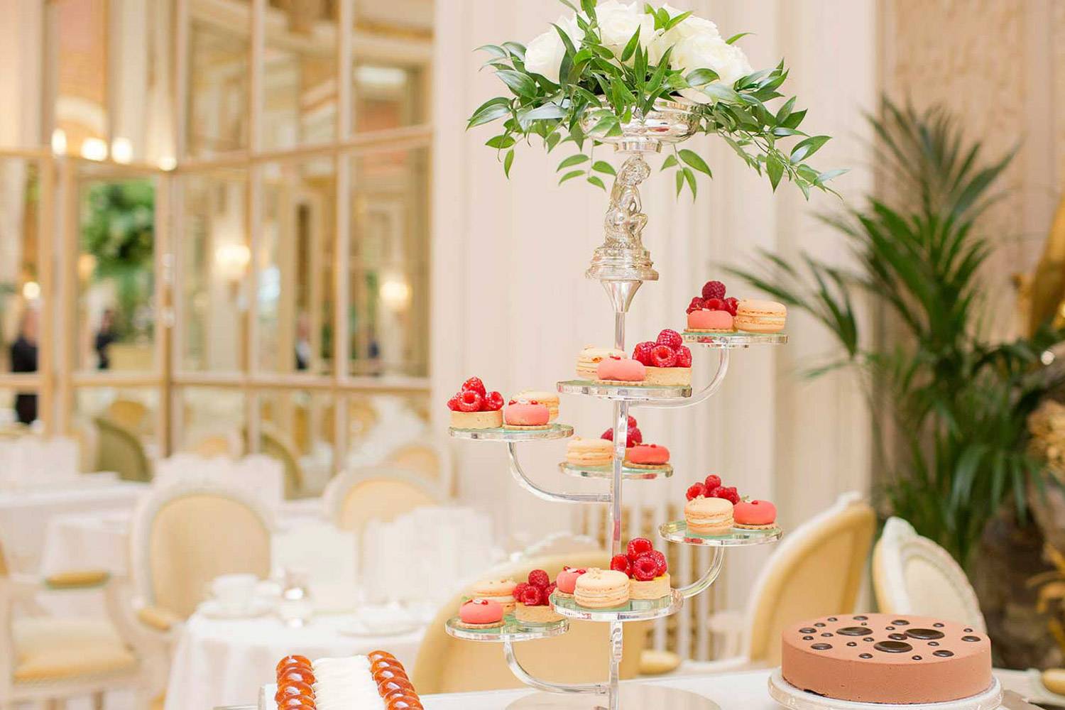 An image of dainty pastries, with luxurious dining décor in the background at The Ritz London.