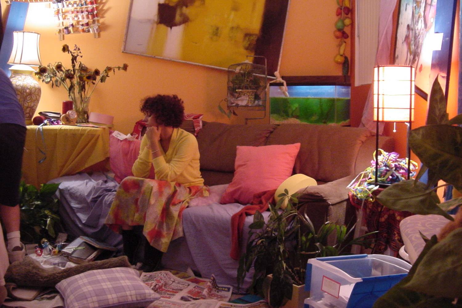 Image of a woman sitting on a couch in a messy and chaotic room 