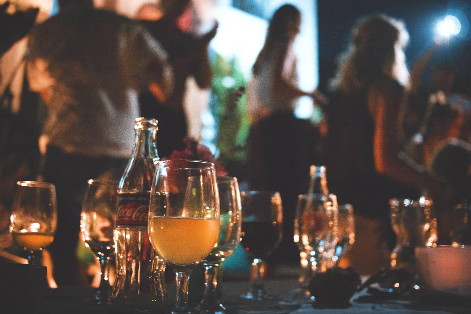 Image of bottles of beer and glasses on a table with people in the background