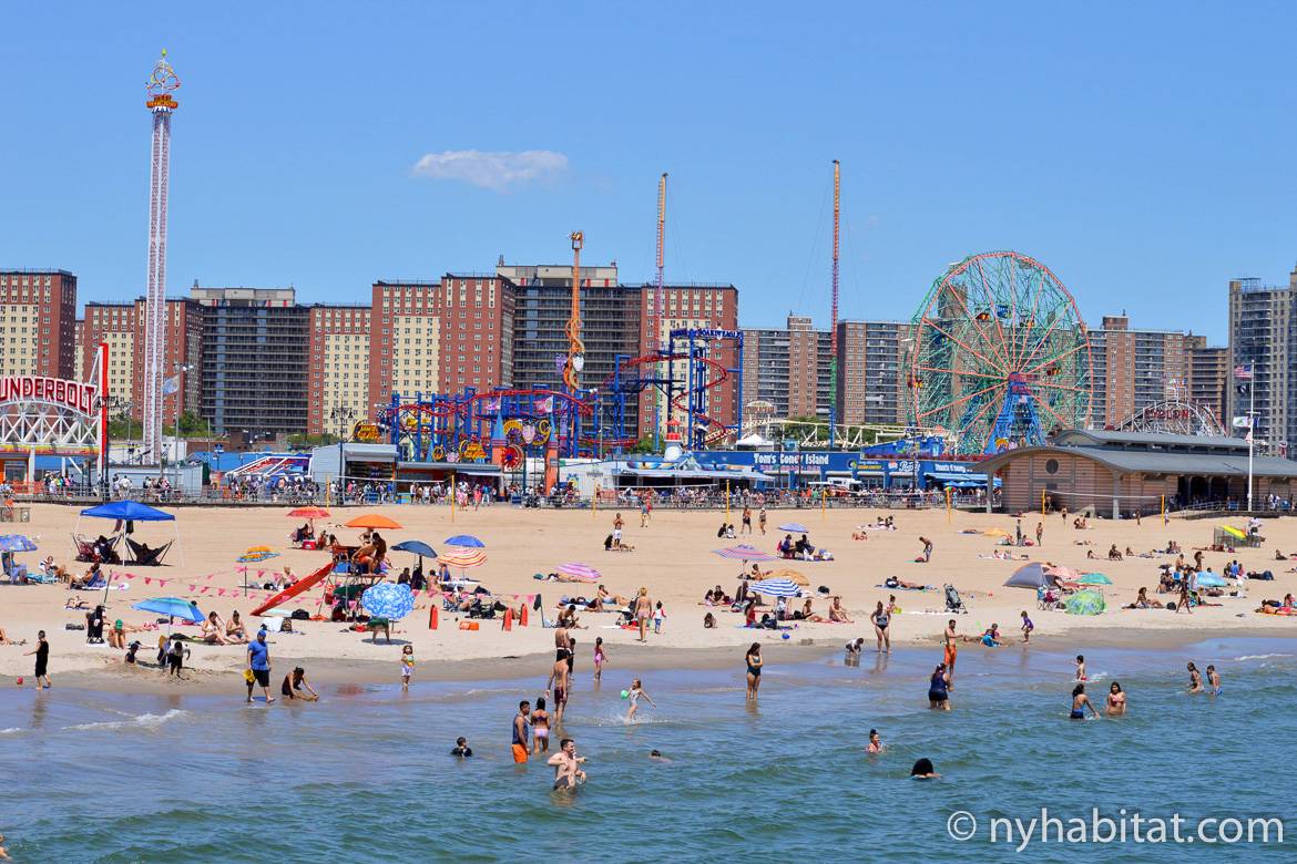Bild vom Strand in Coney Island mit Schwimmern, der Strandpromenade und Luna Park im Hintergrund.