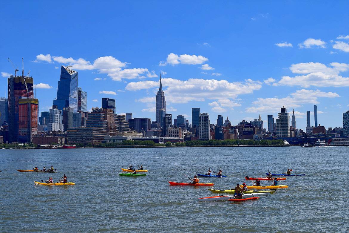 Bild von Menschen, die in New York City auf dem Fluss Kajak fahren mit der Skyline der Stadt im Hintergrund.