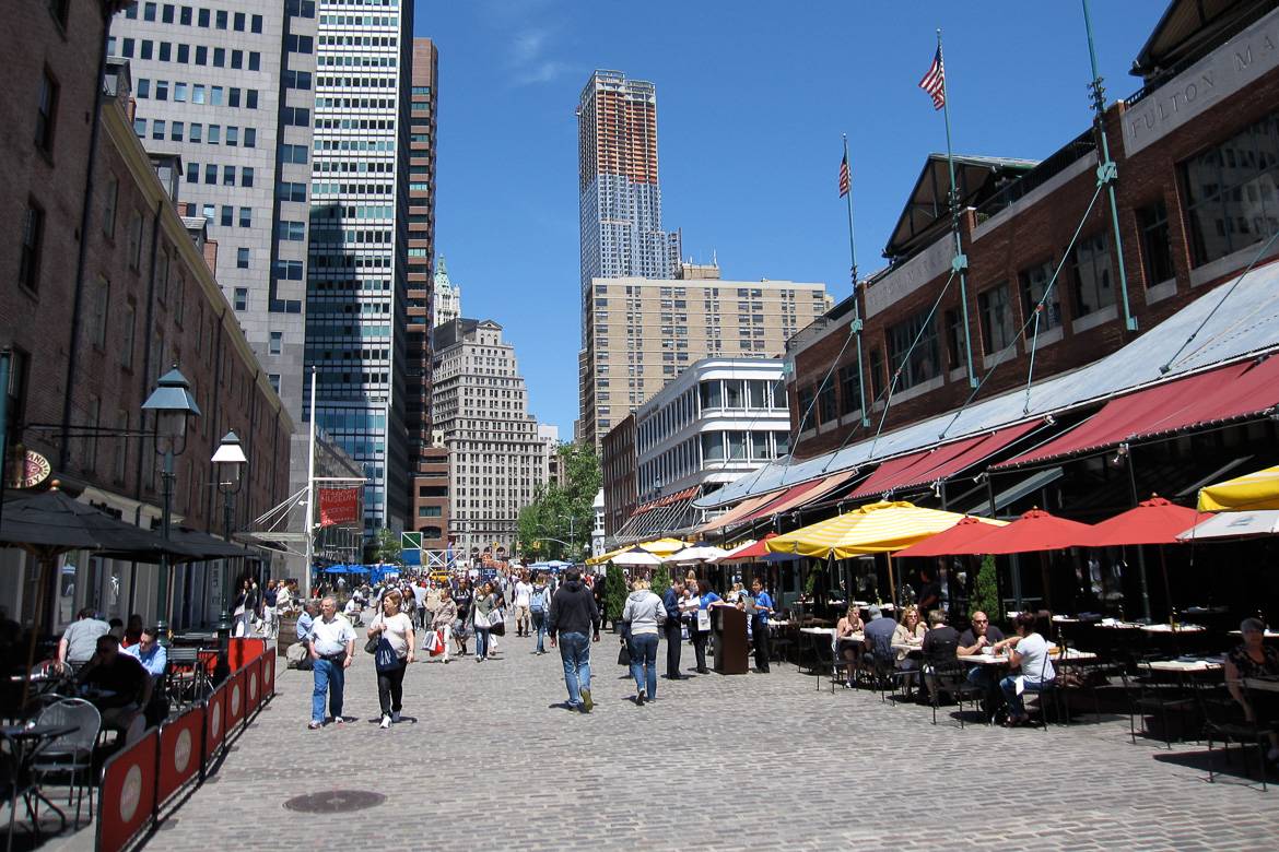 Bild von South Street Seaport an einem sonnigen Tag, gefüllt mit Tischen und Menschen, die draußen essen.