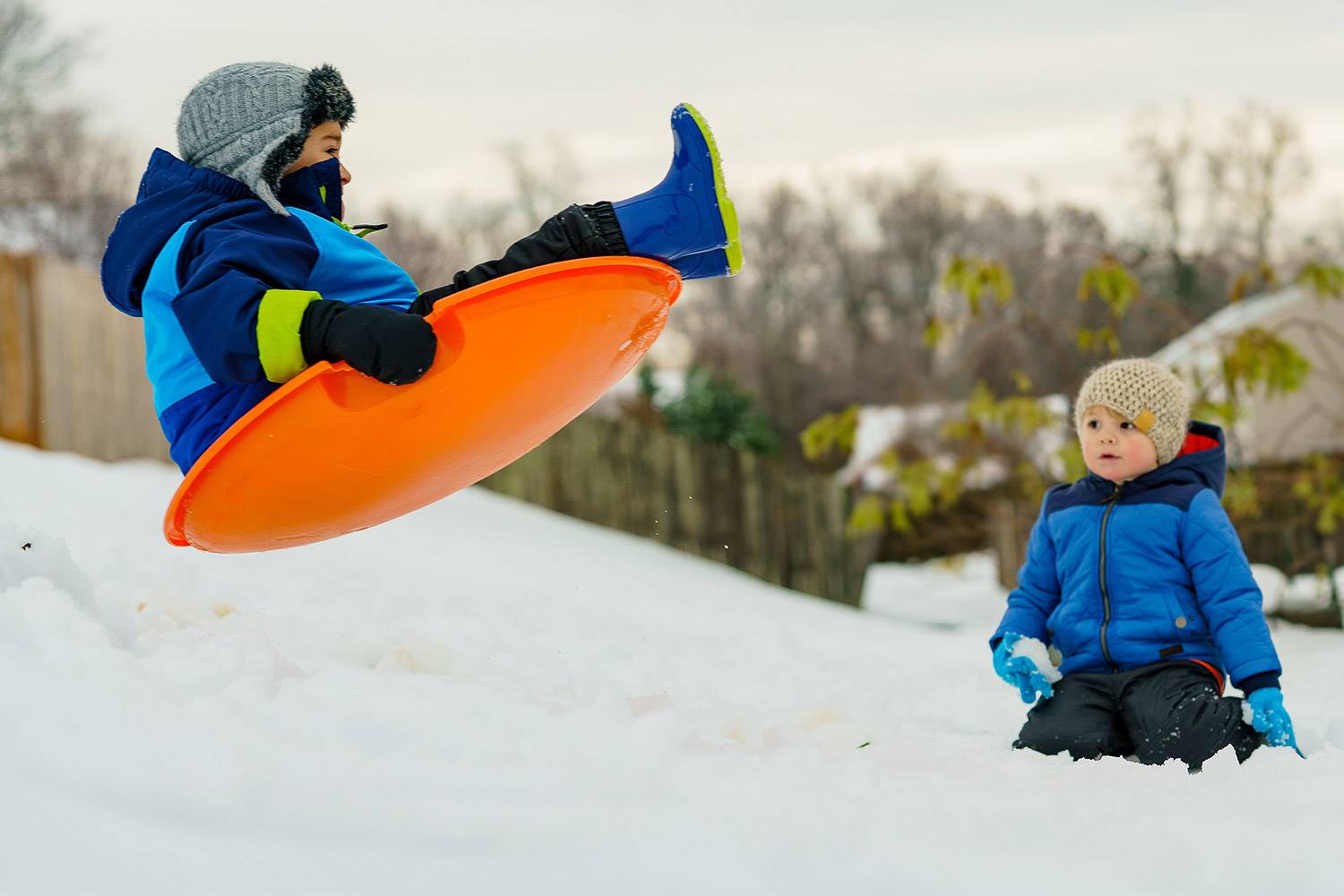 Bild eines Jungen, der im Schnee mit seinem Schlitten durch die Luft fliegt, während ein anderes Kind zuschaut (Bild: Unsplash)