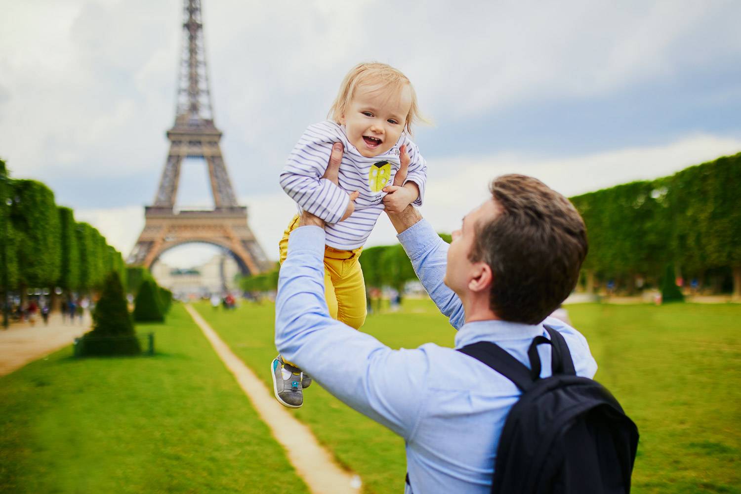 Bild eines Vaters, der sein Baby in der Luft hält mit dem Eiffelturm im Hintergrund