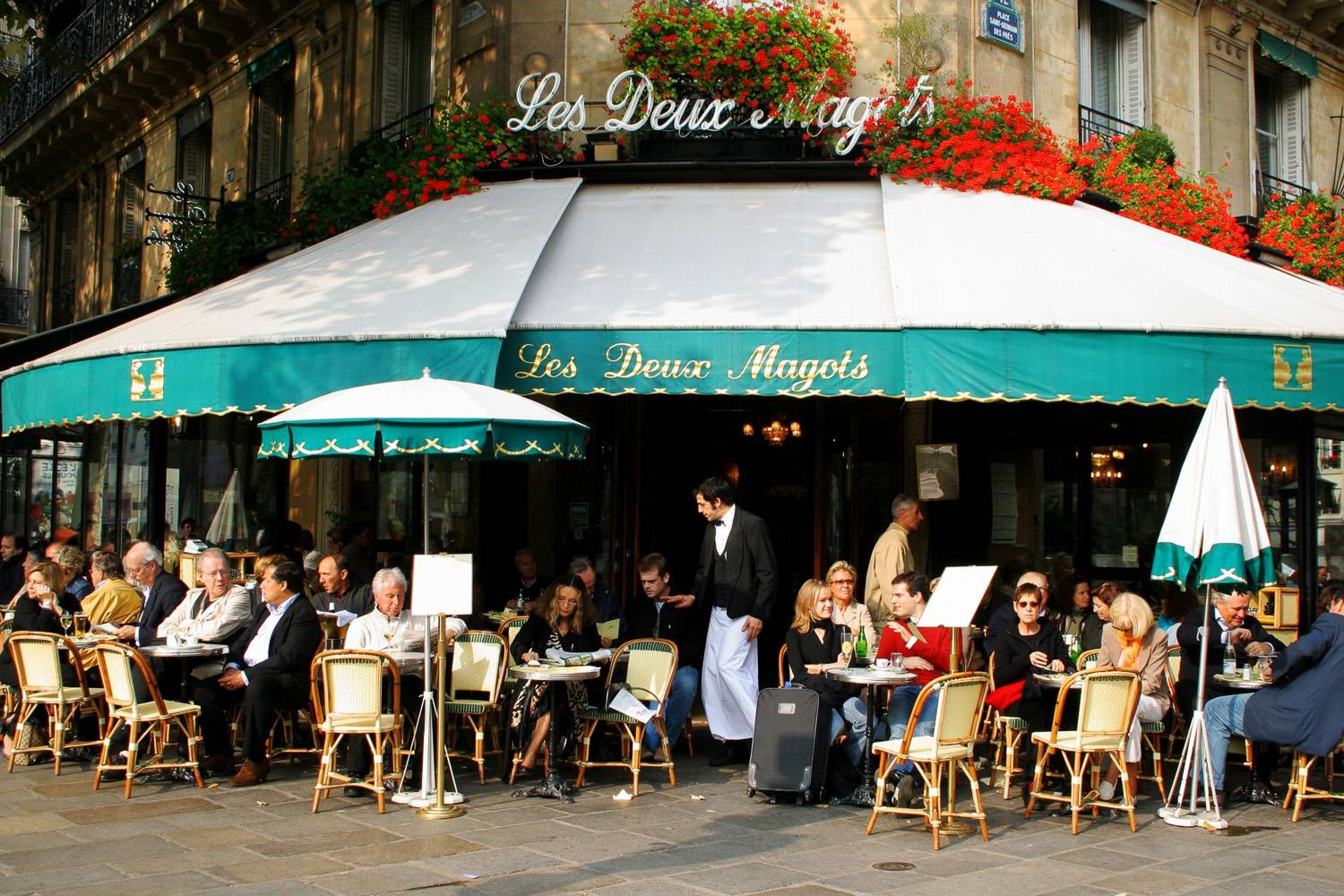Bild des Eingangs des Restaurants Les Deux Magots in Paris mit Menschen, die an den Tischen draußen sitzen