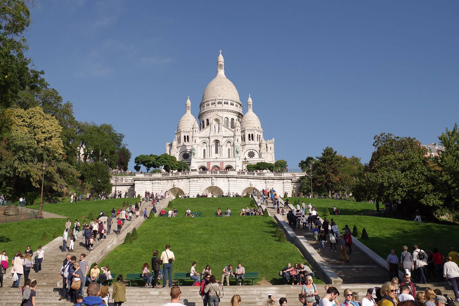 Bild der Sacre Coeur Basilika in Paris mit Menschen, die die Treppen besteigen, die auf den Hügel führen