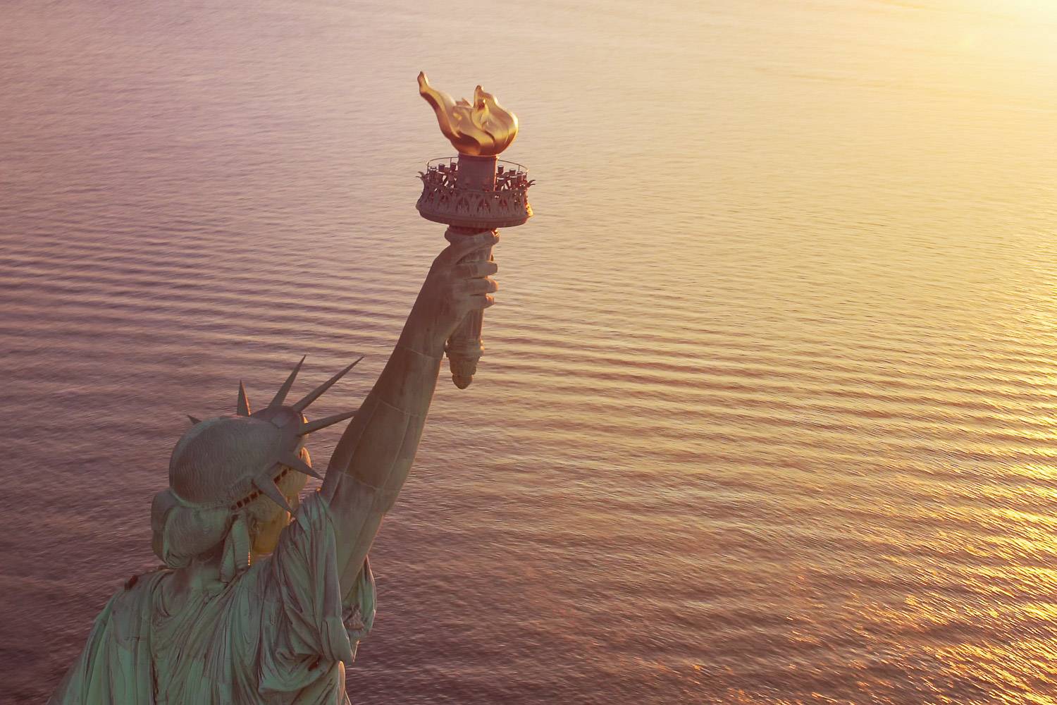 Image de la Statue de la Liberté au coucher du soleil, avec sa torche dorée en gros plan au-dessus de l'eau