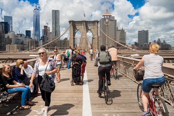 Bild mit Menschen, die auf der Brooklyn Bridge Rad fahren, mit dem Freedom Tower im Hintergrund