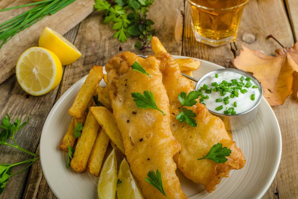 Photo de poisson passé sur une assiette de frites avec sauce tartare, fines herbes, citron et bière