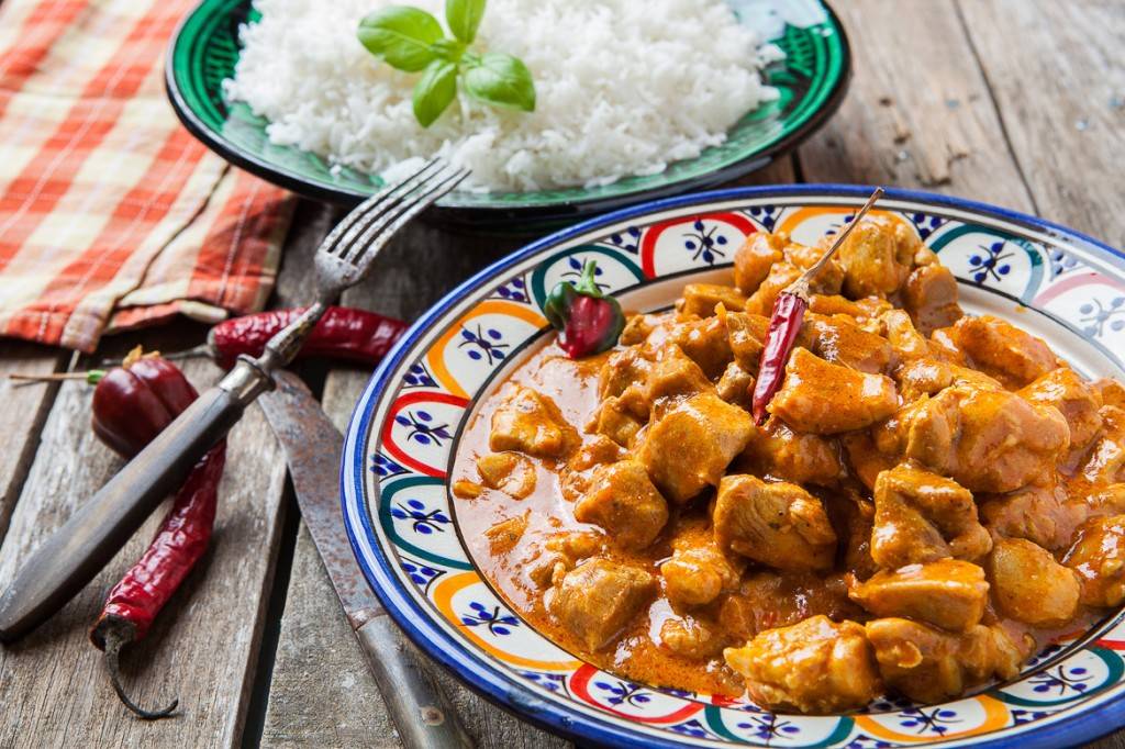 Photo d'une assiette de poulet tikka masala avec son riz et ses piments sur une table en bois