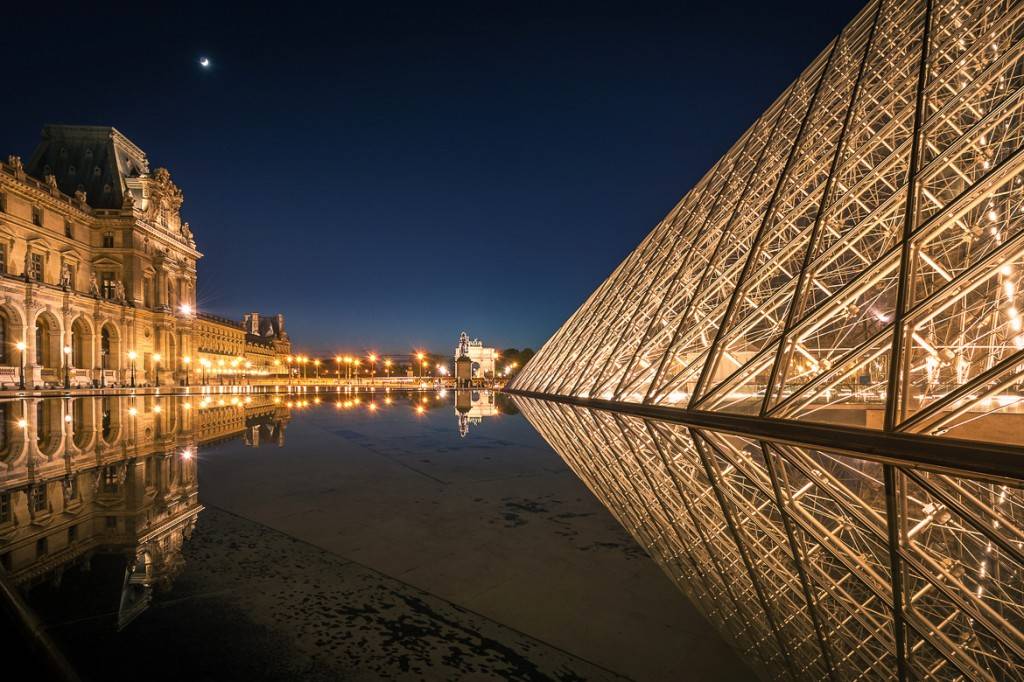 Photo d’une pyramide à côté d’un bassin miroir devant le musée du Louvre