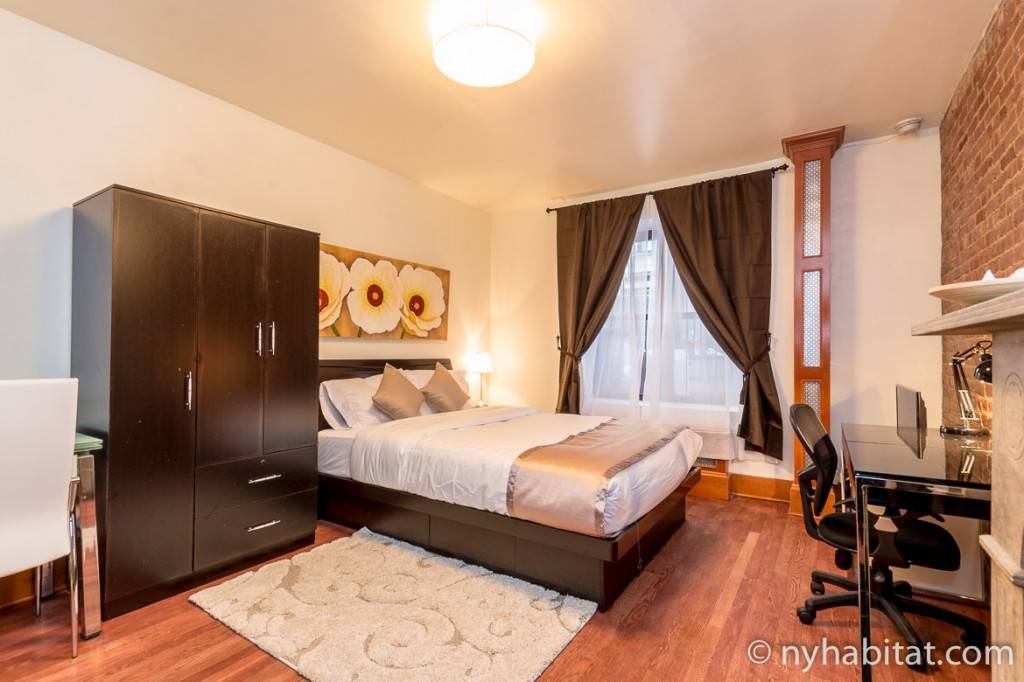 Photo d’une chambre avec ses briques apparentes, sa grande fenêtre et son bureau