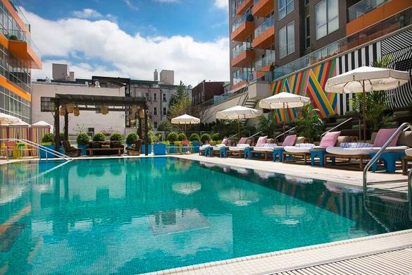 Photographie de la piscine extérieure du McCarren Hotel avec des tables à côté équipées de parasols