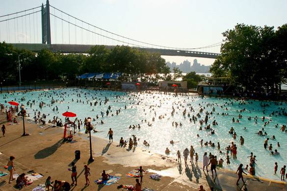 Photographie de personnes en train de se baigner dans la piscine d’Astoria Park avec le Triboro Bridge en arrière-plan