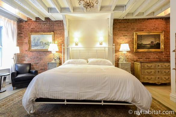 Photo du lit surmonté d’un lustre, avec les murs en pierre apparente en arrière-plan