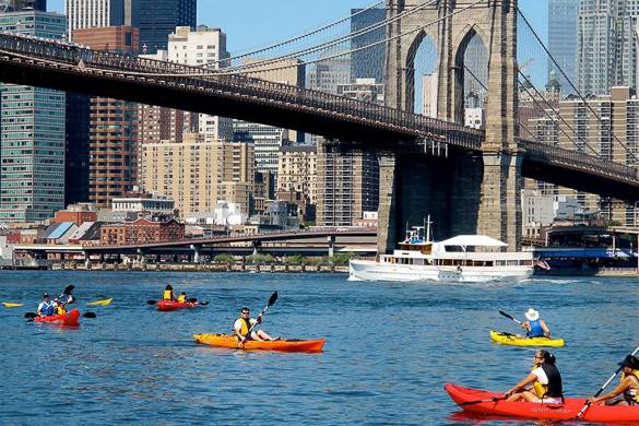 Photo de personnes faisant du kayak sous le pont de Brooklyn avec la vue de la ville à l’horizon.