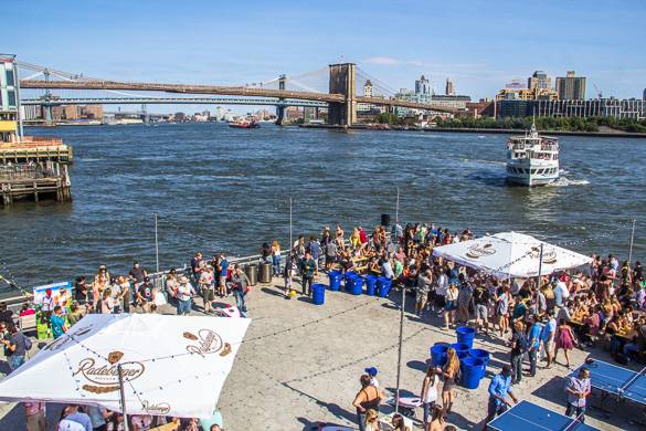 Photo d’un festival en plein air au bord de l’eau avec le pont de Brooklyn et un ferry en arrière-plan