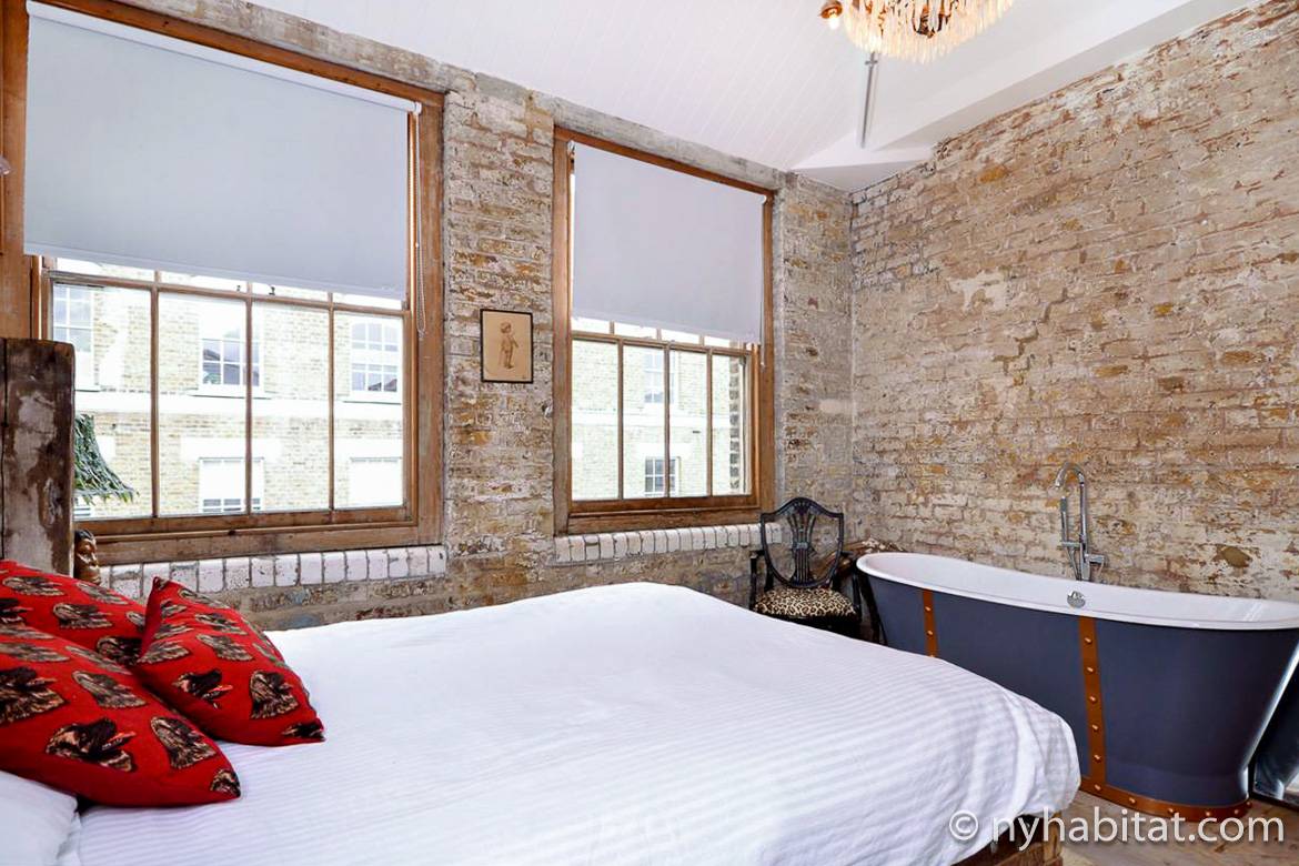 Photo de la chambre de l’appartement LN-573 avec briques apparentes et baignoire ancienne.