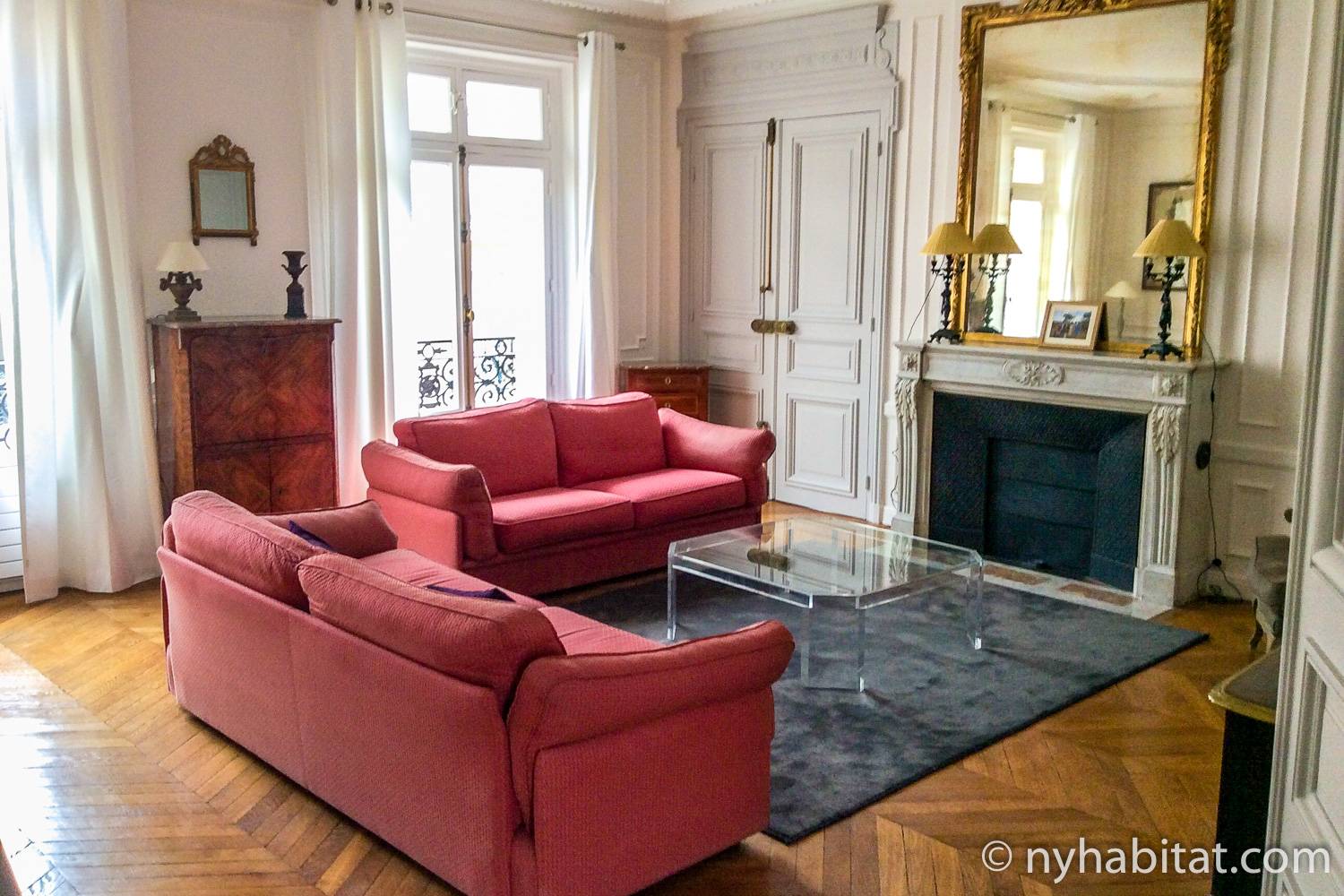 Photo du salon de l’appartement PA-3348 avec une cheminée décorative, des portes-fenêtres et un canapé rouge.