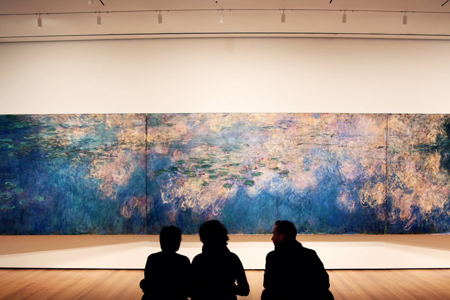 Photo de personnes assises devant le tableau Reflets de nuages sur l'étang aux nénuphars de Claude Monet.