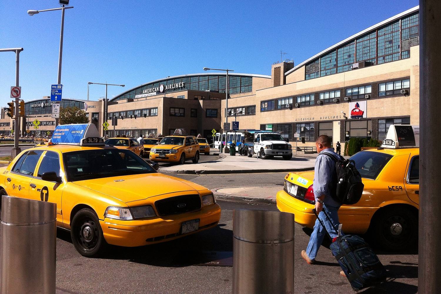Photo de taxis jaunes attendant des voyageurs à l’entrée de l’aéroport LaGuardia et d’un voyageur avec une valise.