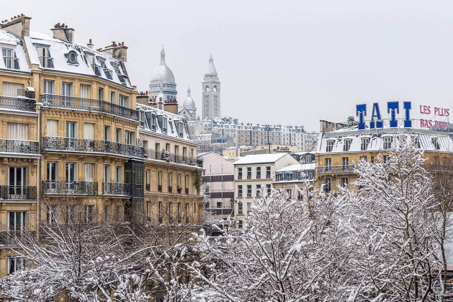 Photo de bâtiments haussmanniens aux toits enneigés.