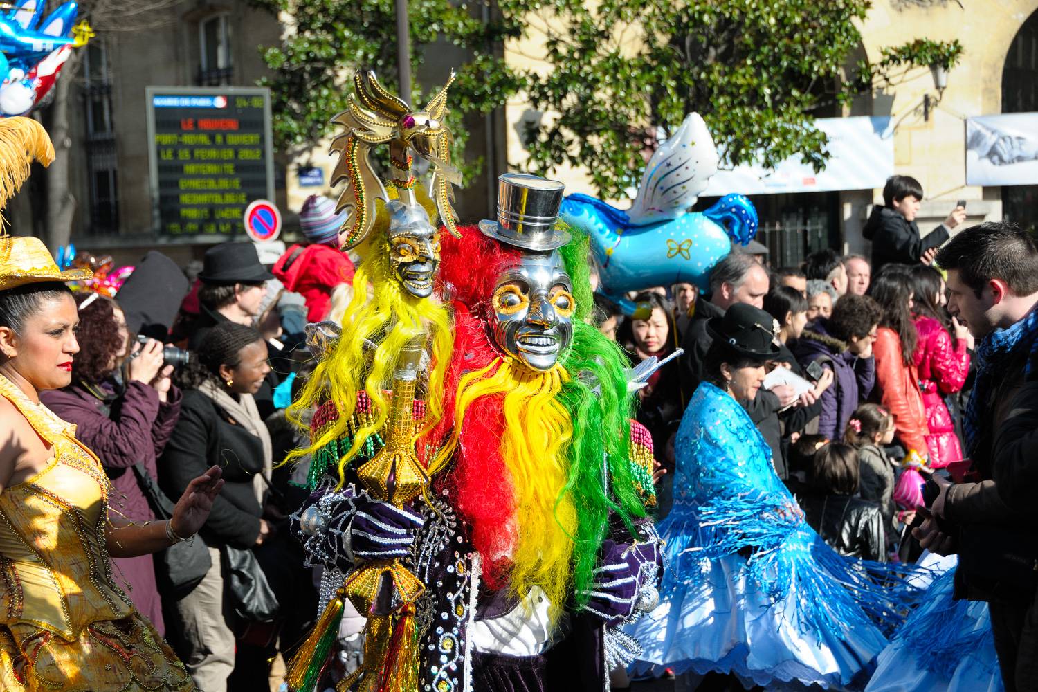 Photo de personnes portant des masques et des perruques aux couleurs éclatantes en train de défiler lors de la parade du Carnaval de Paris.