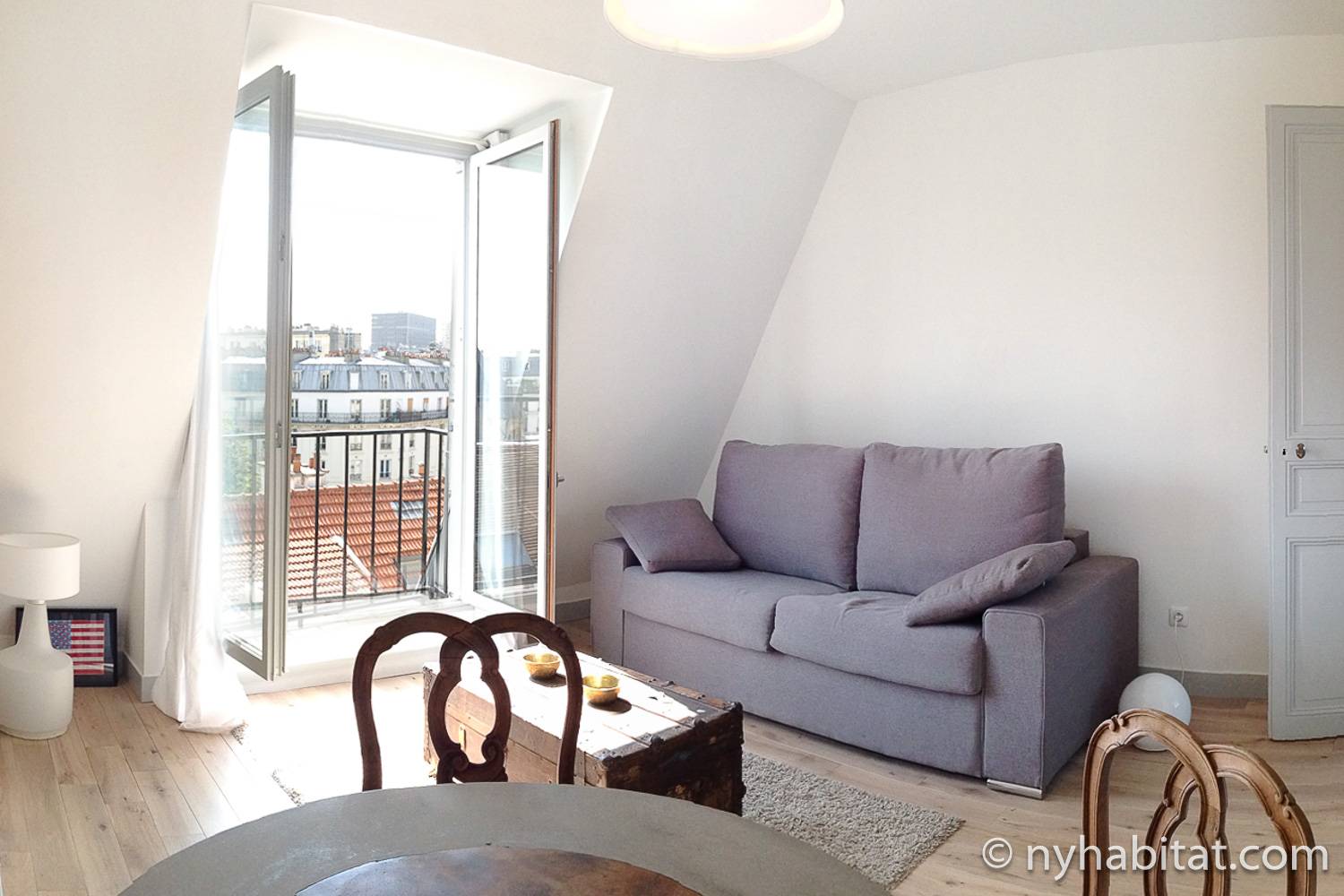 Photographie du salon de l’appartement PA-4561 dans le Quartier latin à Paris avec un canapé gris et des fenêtres.