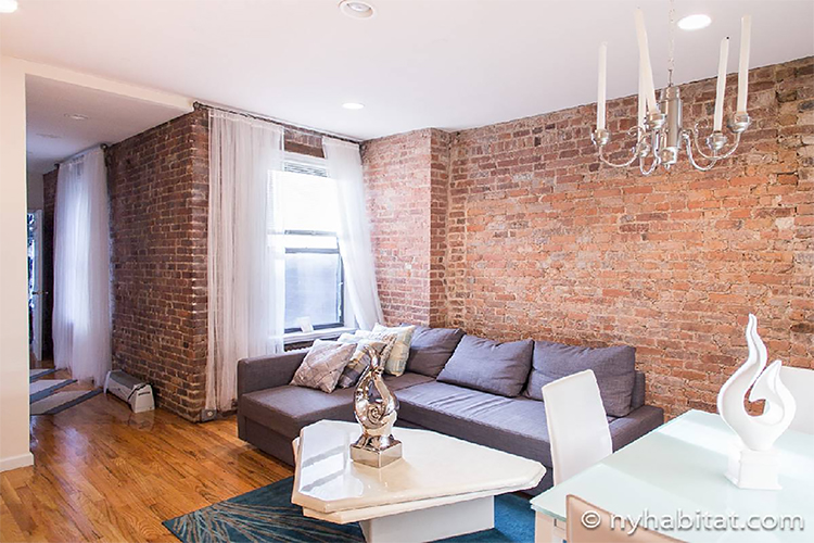 Photo d’un appartement T4 meublé (NY-1587) avec canapé gris, lustre et décorations aux couleurs chaleureuses.